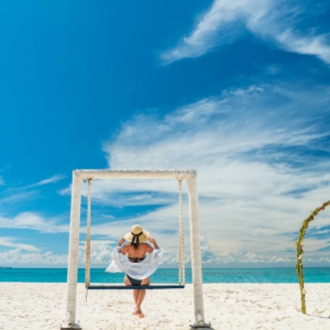 Young woman with hat on a swing in front of beautifull Indian Ocean tropical beach. Zanzibar vacation